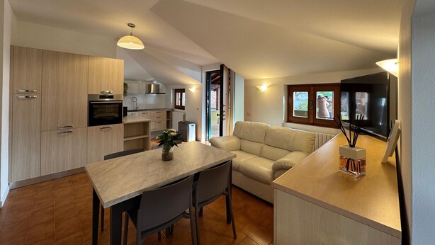A modern kitchen with wooden cabinets, a dining table, and a sofa in a living area. - Apartment with large panoramic terrace (Traona)