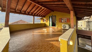 A spacious balcony with wooden beams, a brick floor, and a view of a mountain landscape. - Apartment with large panoramic terrace (Traona)
