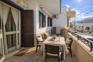 A balcony with a table set for two, a potted plant, and a TV. - Beach House 50m from the Sea | 2 Bedrooms, 2 Bathrooms, Air Conditioning (Torre Pali)