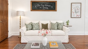 A living room with a white sofa, patterned cushions, a vase with flowers, a lamp, and a framed picture on the wall.