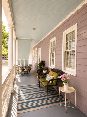 Eine überdachte Veranda mit Streifenmuster, Korbmöbeln und einem Blumentopf.