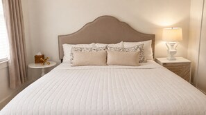 A neatly made bed with a headboard, a bedside table with a lamp, and a window with curtains.