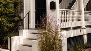 Una casa bianca a due piani con un portico, una porta nera e una scala che conduce al secondo piano.