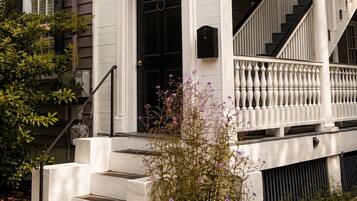 A white two-story house with a front porch, a black door, and a staircase leading to the second floor.