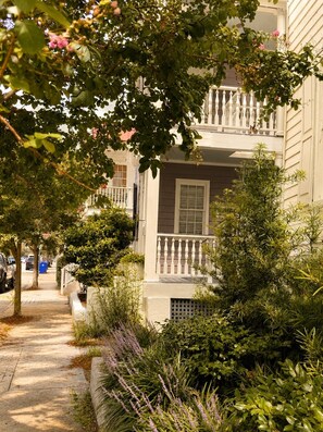 A residential street with a two-story house featuring a balcony with a white balustrade. - The Fig House on Spring · Walk to King · 3BR, Sleeps 8 (Charleston)