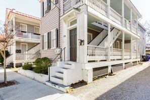 A two-story building with a porch, a staircase, and a small garden area. - The Fig House on Spring · Walk to King · 3BR, Sleeps 8 (Charleston)