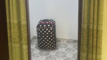 Quarto com cortinas estampadas, chão ladrilhado e uma mala com bolinhas num canto.