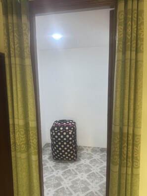 Una habitación con cortinas estampadas, piso de baldosas y una maleta de lunares en la esquina.