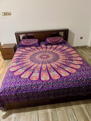 Una cama con una colcha estampada, un cabecero de madera y una mesita de noche con un cajón.