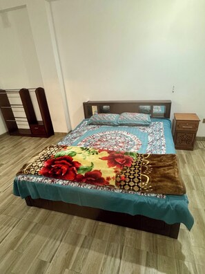 Una cama con cubrecama floral, cabecera de madera y mesita de noche con cajón.