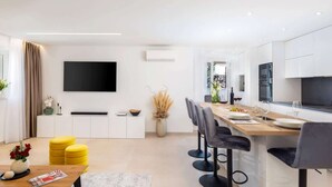 Una cocina moderna con comedor, un televisor de pantalla plana en la pared y un conjunto de taburetes de bar.