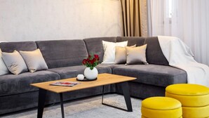 Una sala de estar moderna con un sofá gris, una mesa de centro de madera, otomanas amarillas y una lámpara de pie.