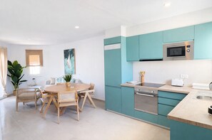 A modern kitchen with teal cabinets, a microwave, and a toaster. There is a dining area with a wooden table and chairs. - Brisa del Mar 54 (Los Delfines)