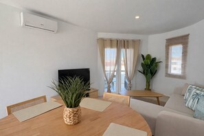 A living room with a TV, a dining table with chairs, a sofa, and a large window with curtains. - Brisa del Mar 54 (Los Delfines)