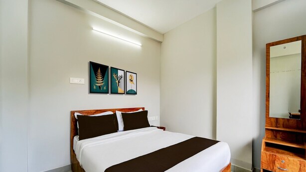 Ein Schlafzimmer mit einem hölzernen Bett, weißer Bettwäsche, einem Nachttisch, einem Spiegel und drei an der Wand befestigten Kunstwerken.