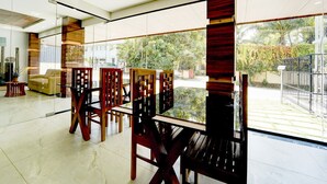 A modern dining area with glass partitions, wooden chairs, and a view of the outdoors. - Deluxe Super Townhouse Oak Cochin (Aluva)
