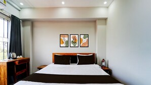 A hotel room with a large bed, a wooden nightstand, a desk with a kettle, and three framed artworks on the wall. - Deluxe Super Townhouse Oak Cochin (Aluva)
