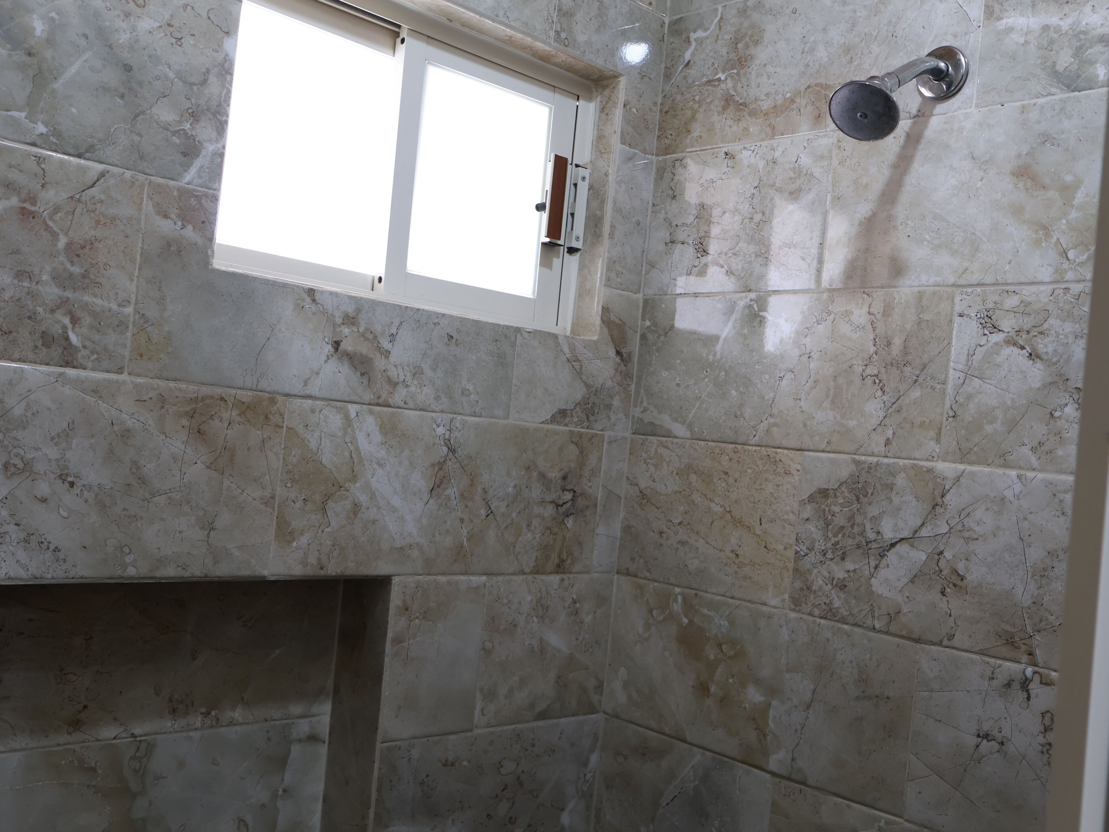 A bathroom with marble tiles, a window, and a shower.
