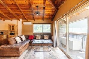 A cozy living room with a wooden ceiling, a sofa with patterned cushions, a coffee table, and a large window with blinds. - Hotel Casa Patrón Parras  (Parras de la Fuente)