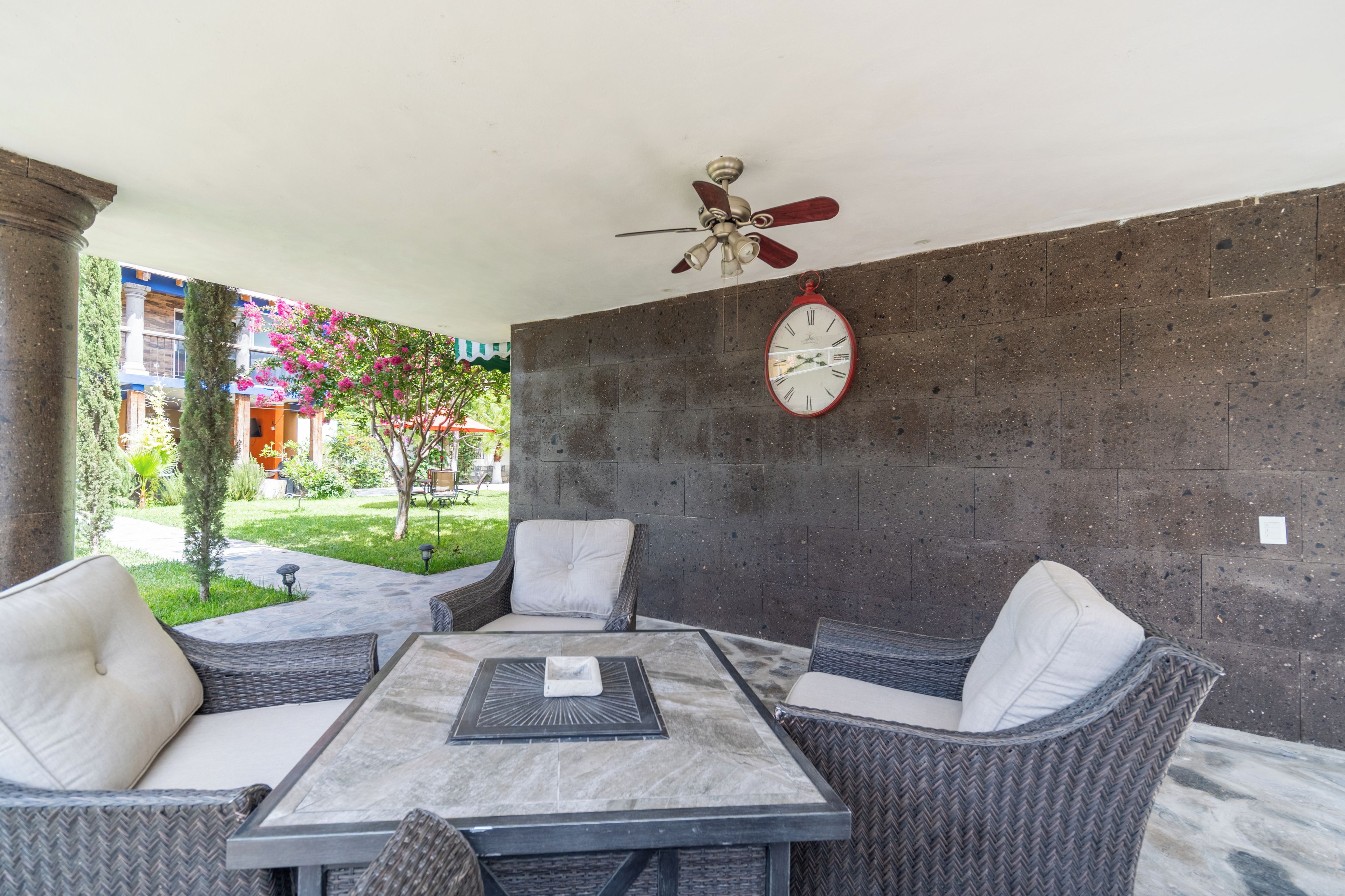 A patio area with a table and chairs, a wall clock, and a ceiling fan.
