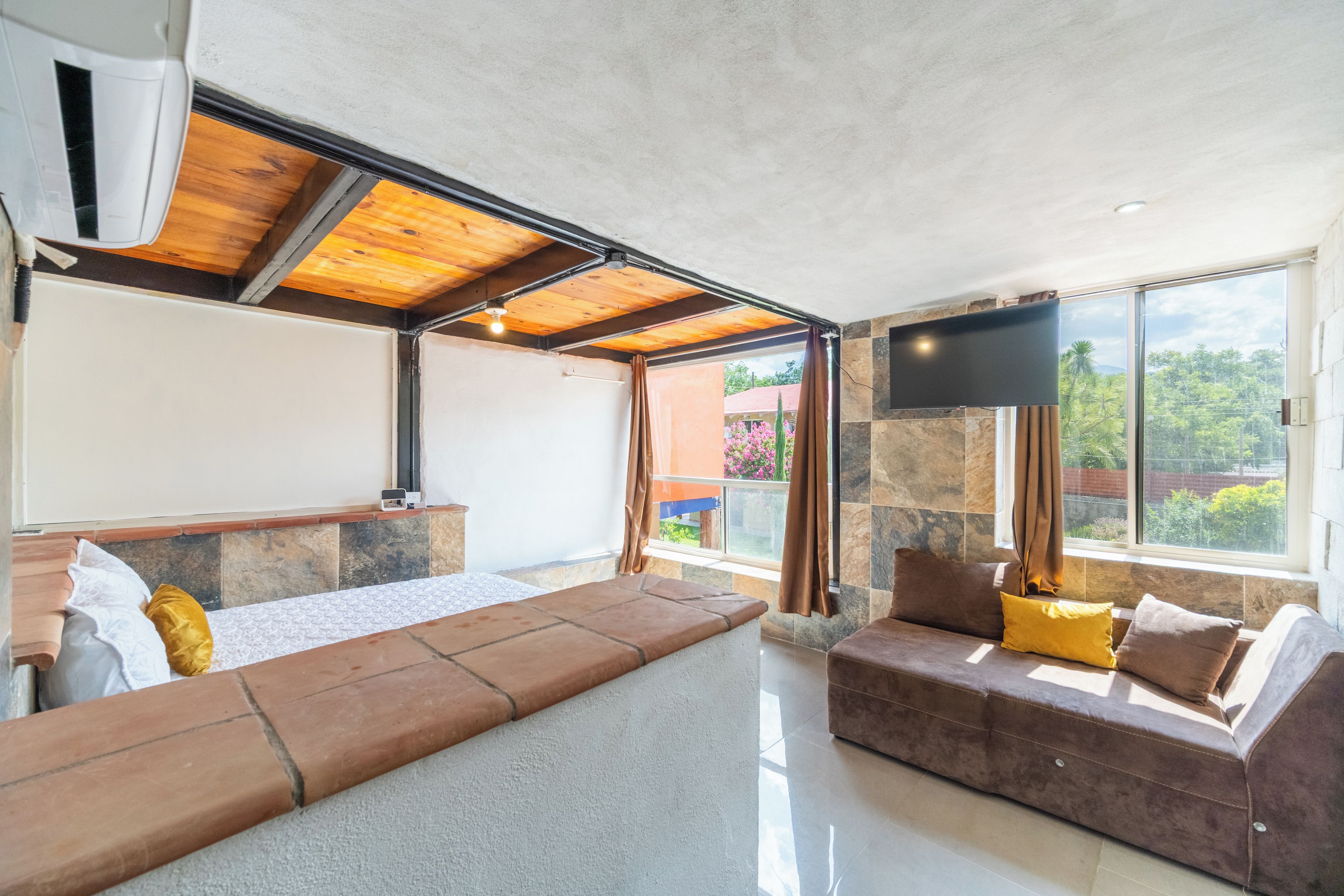 A modern living room with a sofa, a flat-screen TV, and a large window offering a view of greenery.