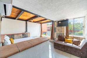 A modern living room with a sofa, a flat-screen TV, and a large window offering a view of greenery. - Hotel Casa Patrón Parras  (Parras de la Fuente)