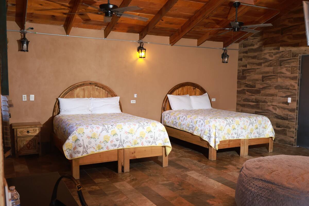 A room with two wooden beds, a stone wall, and a ceiling fan.
