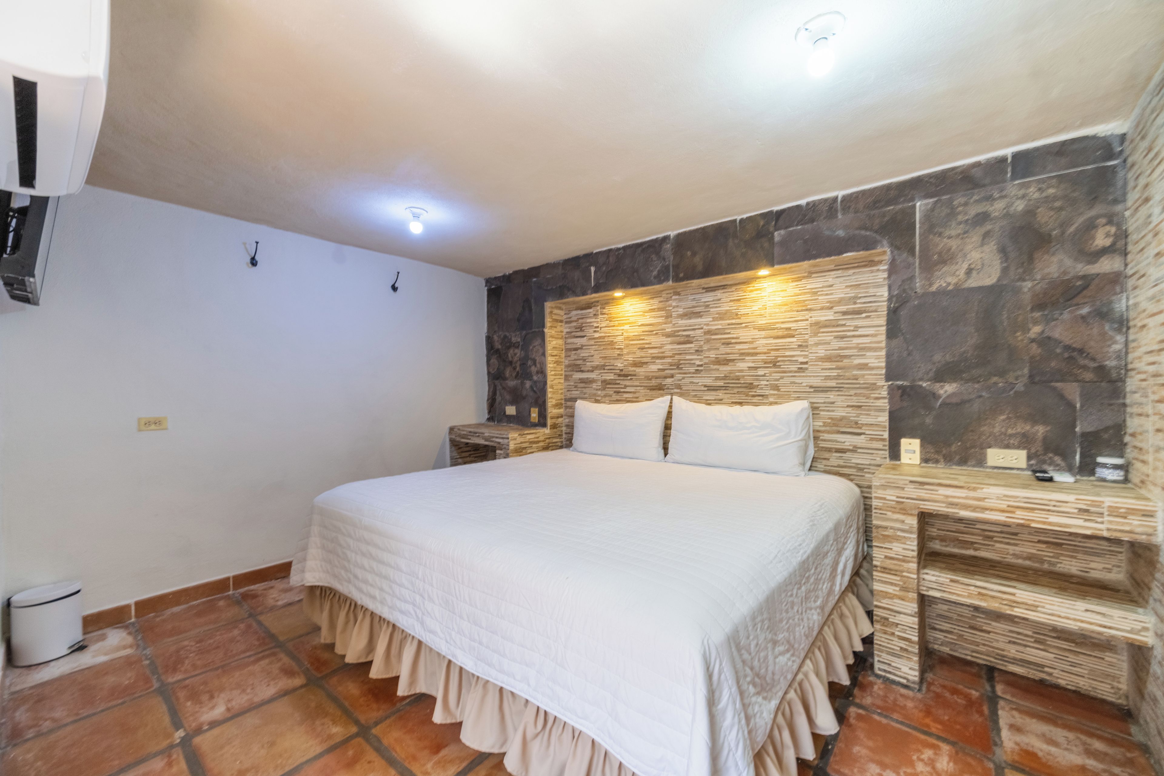 A bedroom with a large bed, a stone accent wall, and a tiled floor.