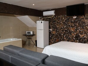 A hotel room with a bed, a small table with a microwave, a refrigerator, a sofa, and a stone-patterned wall.
