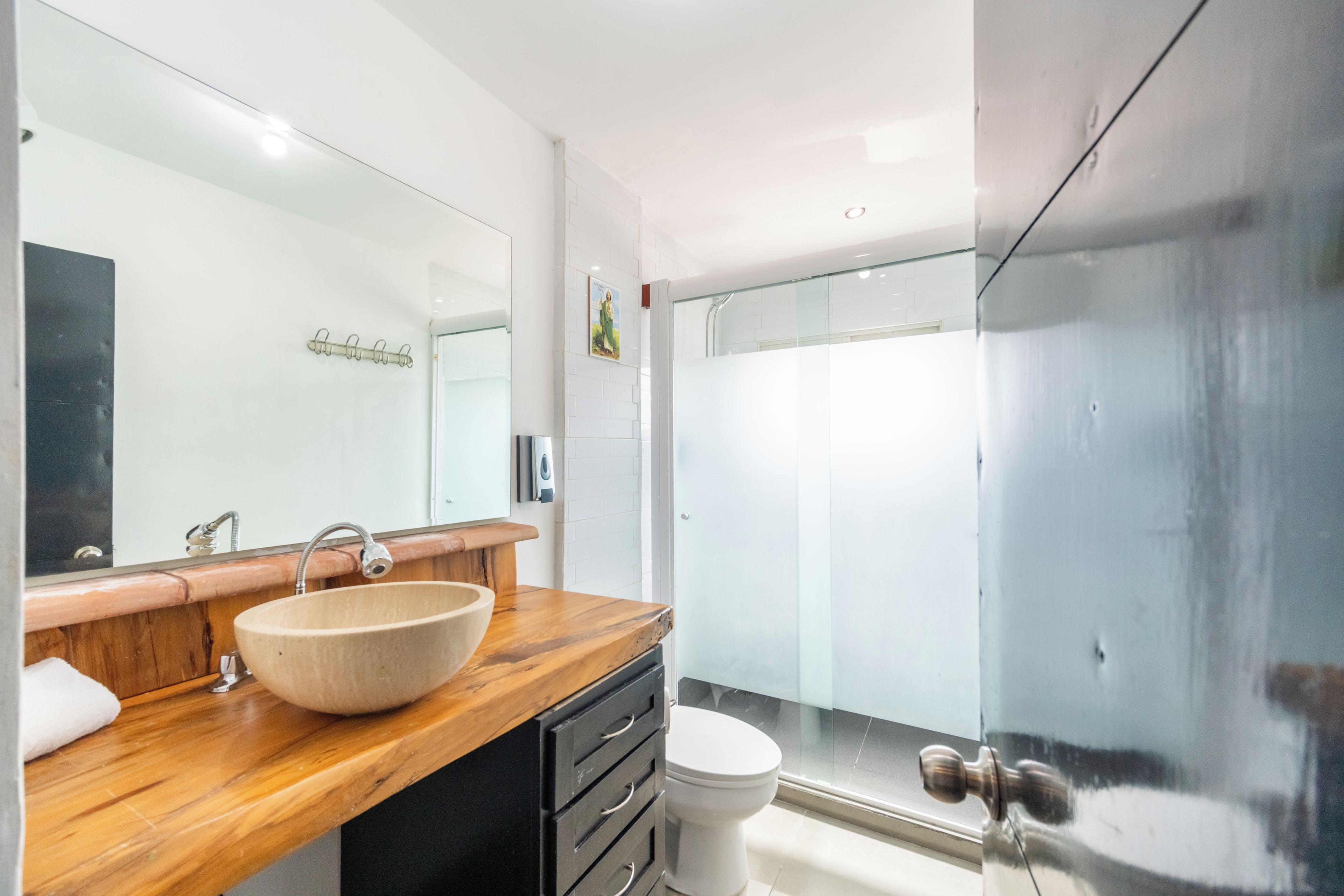 A modern bathroom with a wooden vanity, a large mirror, a white sink, and a glass shower enclosure.