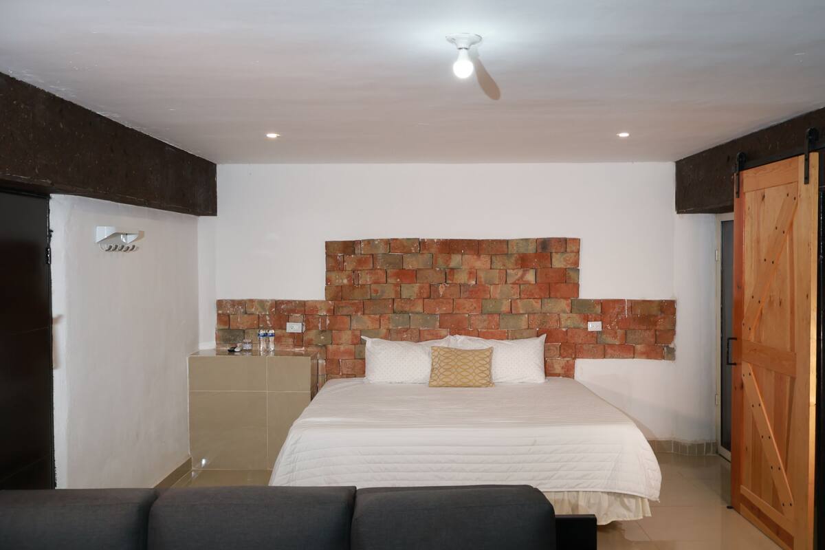 A bedroom with a brick-patterned headboard, a bed with white bedding, a ceiling fan, and a wooden door.