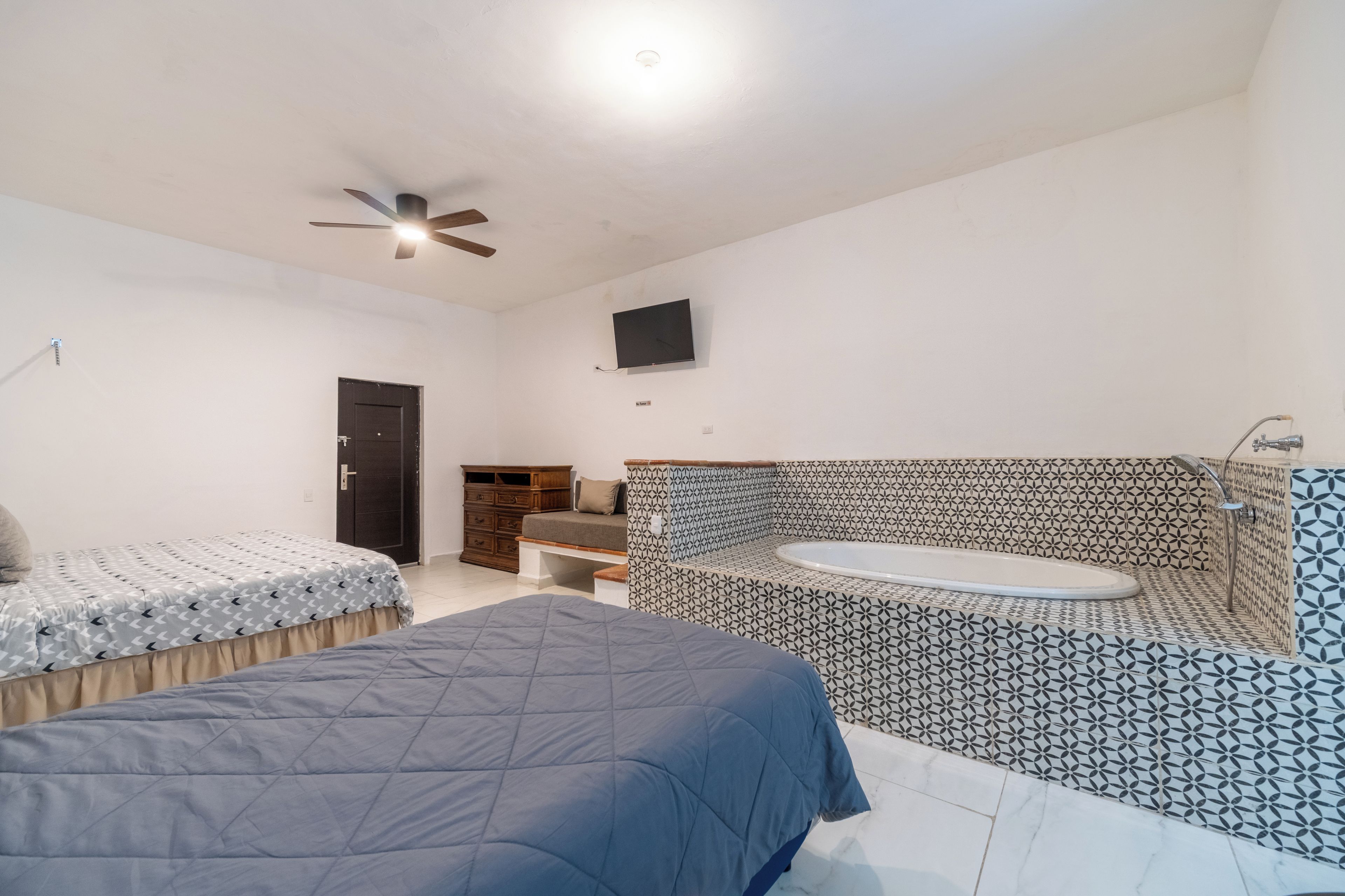 A bedroom with two beds, a dresser, a TV, and a bathroom with a bathtub.