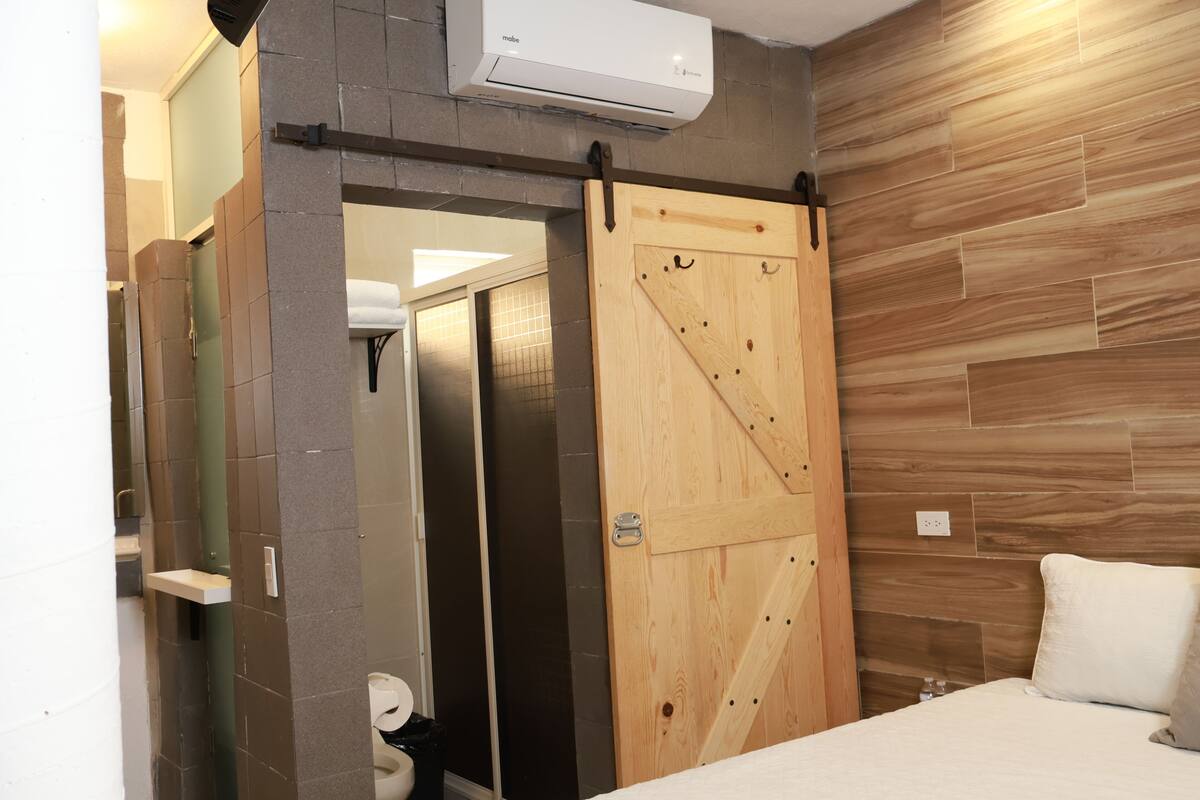 A bathroom with a toilet, a sink, and a shower. There is a sliding door and an air conditioning unit mounted on the wall.