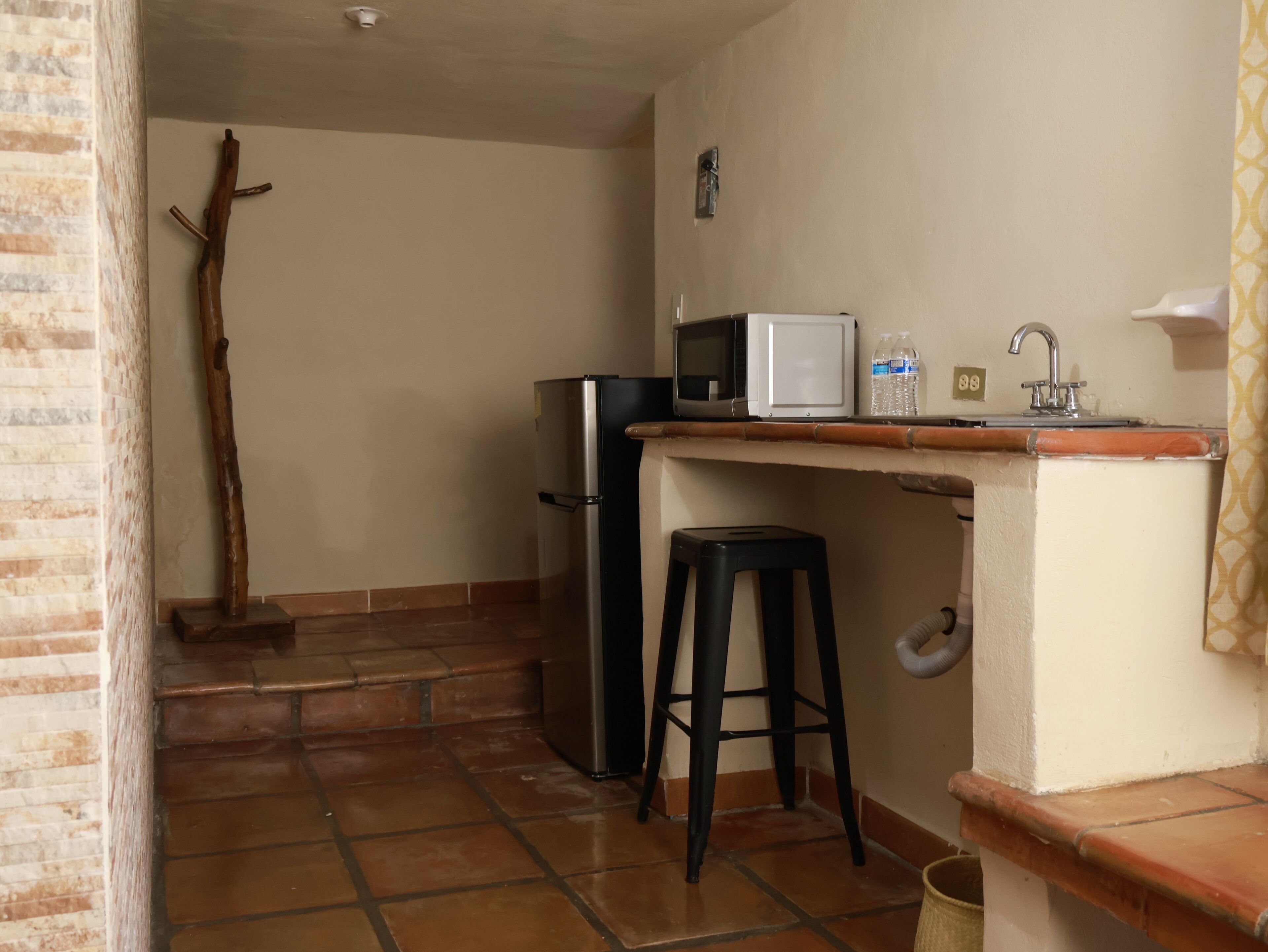 Una cocina compacta con refrigerador, microondas y un taburete pequeño.