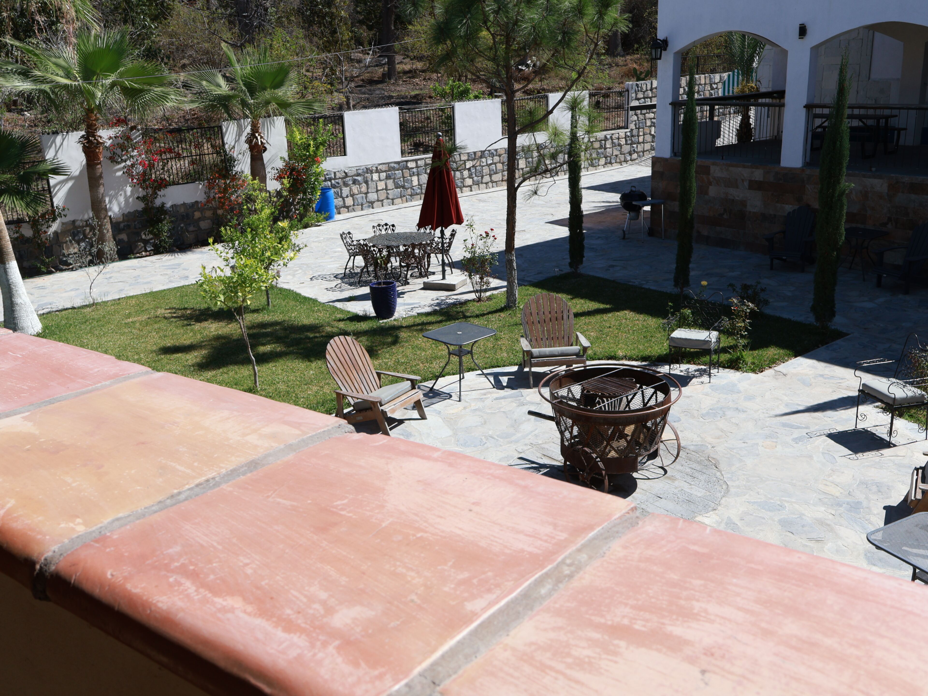 Un patio al aire libre con suelo de piedra, una silla de madera, una parrilla de metal y una mesa con sillas.