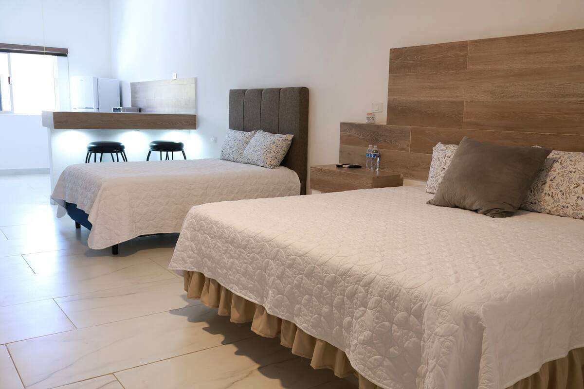 A hotel room with two beds, a wooden headboard, a nightstand, a small table, and a wall-mounted shelf.