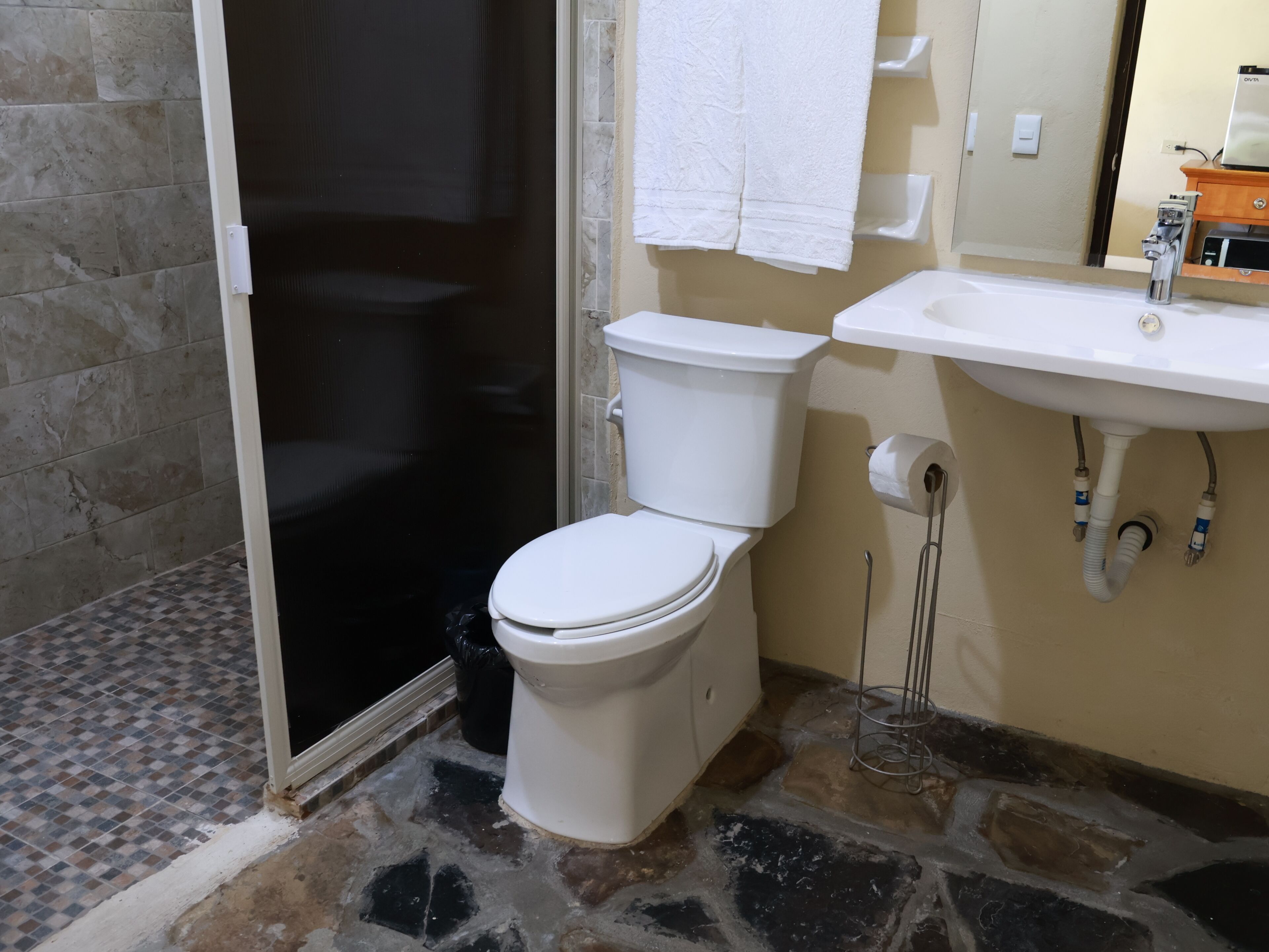 Une salle de bain comprenant des toilettes, un lavabo, un miroir et un espace douche.