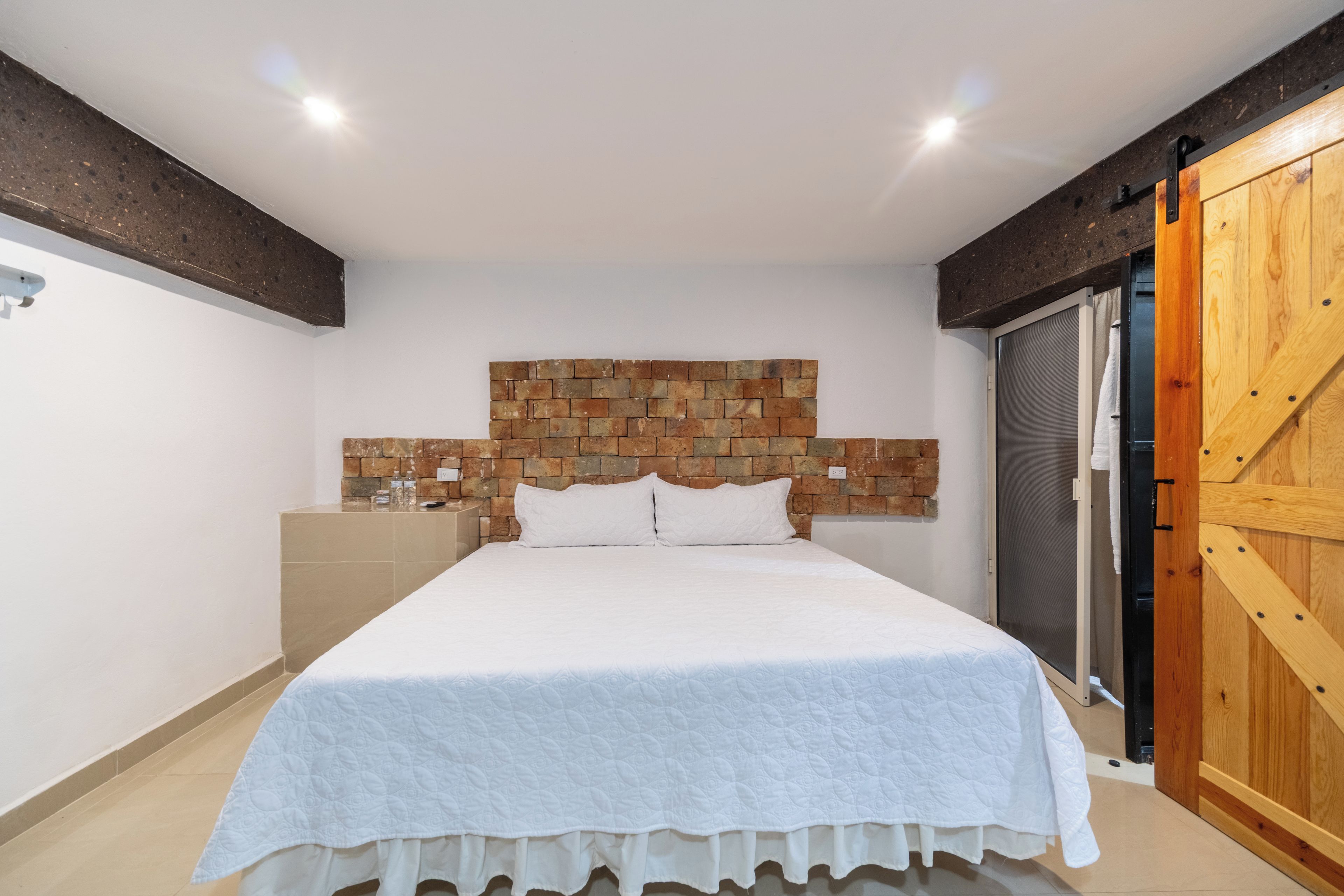 A bedroom with a bed, a stone wall headboard, a wooden door, and a white ceiling.