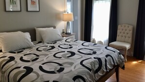 Une chambre à coucher comprenant un lit, une chaise, un ventilateur de plafond, une table de chevet avec une lampe, et deux tableaux encadrés accrochés au mur.