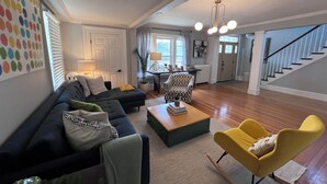 Un vaste salon comprenant un canapé, une table basse et un fauteuil jaune. Un escalier mène à l’étage supérieur.
