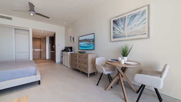 A modern hotel room with a bed, a dining area with chairs, a table, a coffee machine, a TV, and a painting on the wall. - Sonoran Star One (Puerto Peñasco)