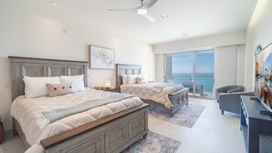 A bedroom with two beds, a ceiling fan, a large window with a view of the ocean, and a balcony with seating. - Sonoran Star One (Puerto Peñasco)