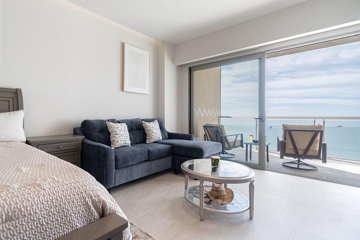Una habitación de hotel moderna con cama, sofá, una mesita y un balcón con vista al mar.