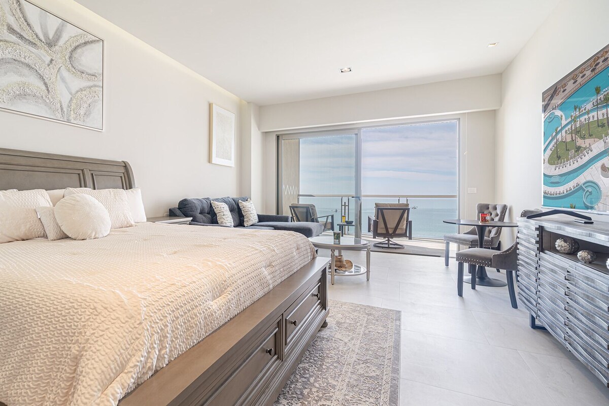 A bedroom with a large bed, a desk, and a view of the ocean.