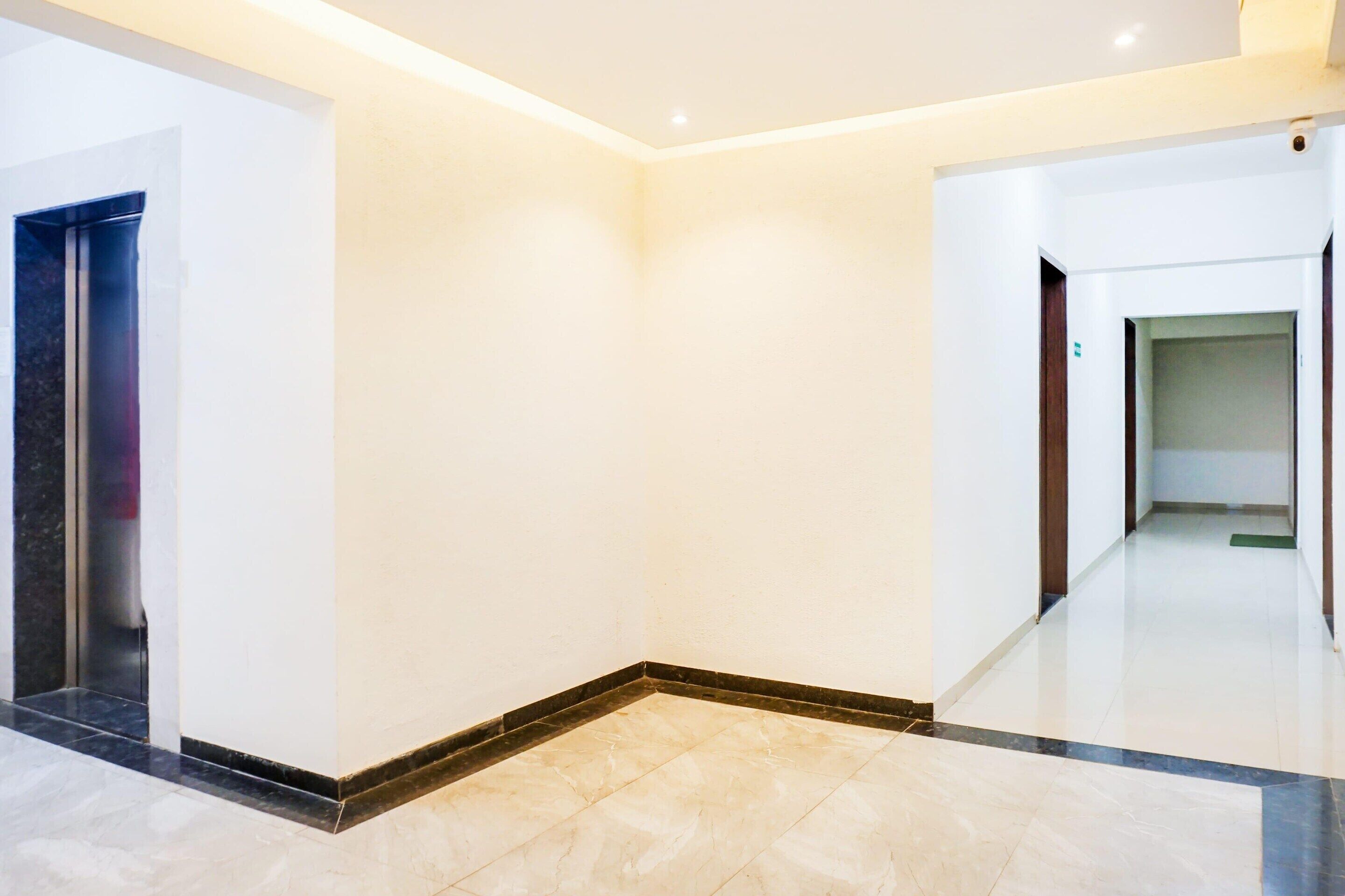 A clean, modern hallway with a marble floor, white walls, and a door on the left.