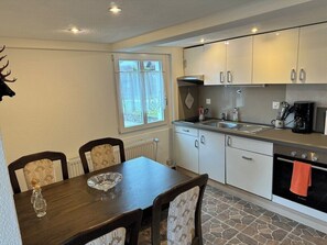 A compact kitchen with a dining table, chairs, a stove, and a window with curtains. - Bijou Lungern 2 (Lungern)