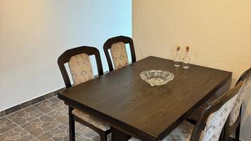 Un coin repas avec une table en bois foncé, quatre chaises dotées de coussins à motifs, une tête de cerf décorative fixée au mur et un sol carrelé en pierre.