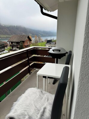 A balcony with a table and chairs, overlooking a lake and houses.