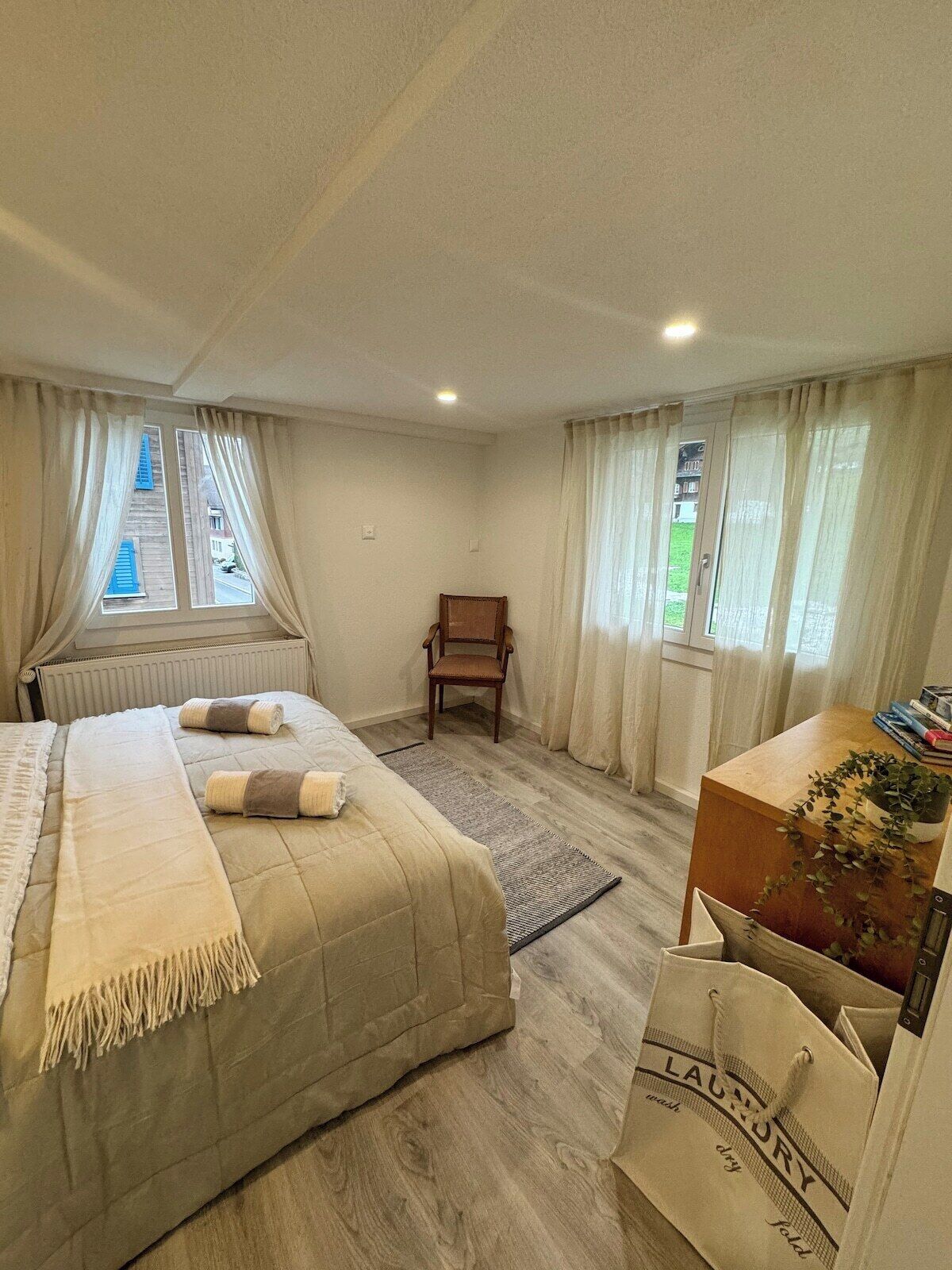 Ein Schlafzimmer mit Bett, Stuhl, Schreibtisch und einem Fenster mit Vorhängen.
