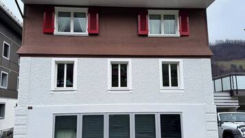 A multi-story building with a flat roof, white exterior walls, and red shutters on the upper windows.